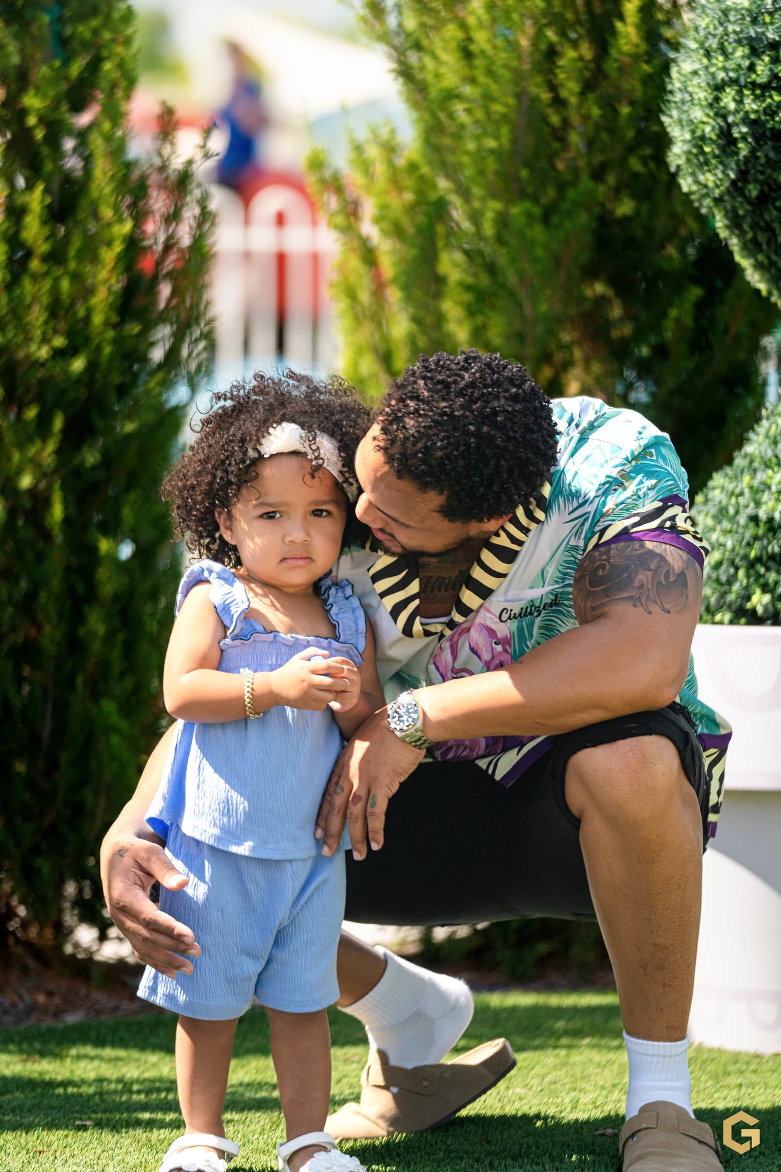 Edgardo kneeling beside his daughter in a quiet garden portrait