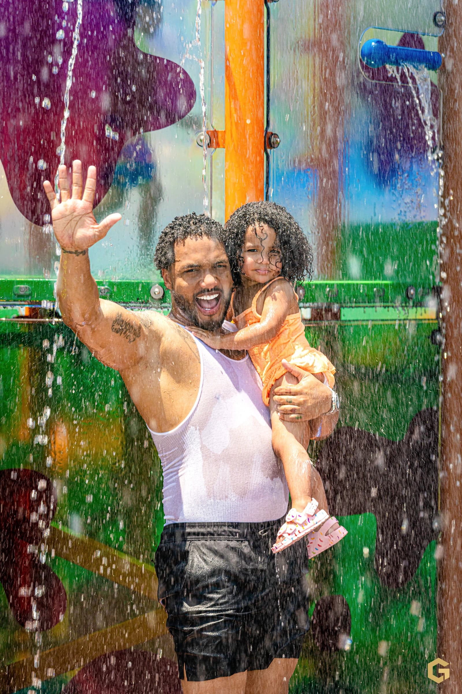 Edgardo waves while holding his daughter beneath the water features