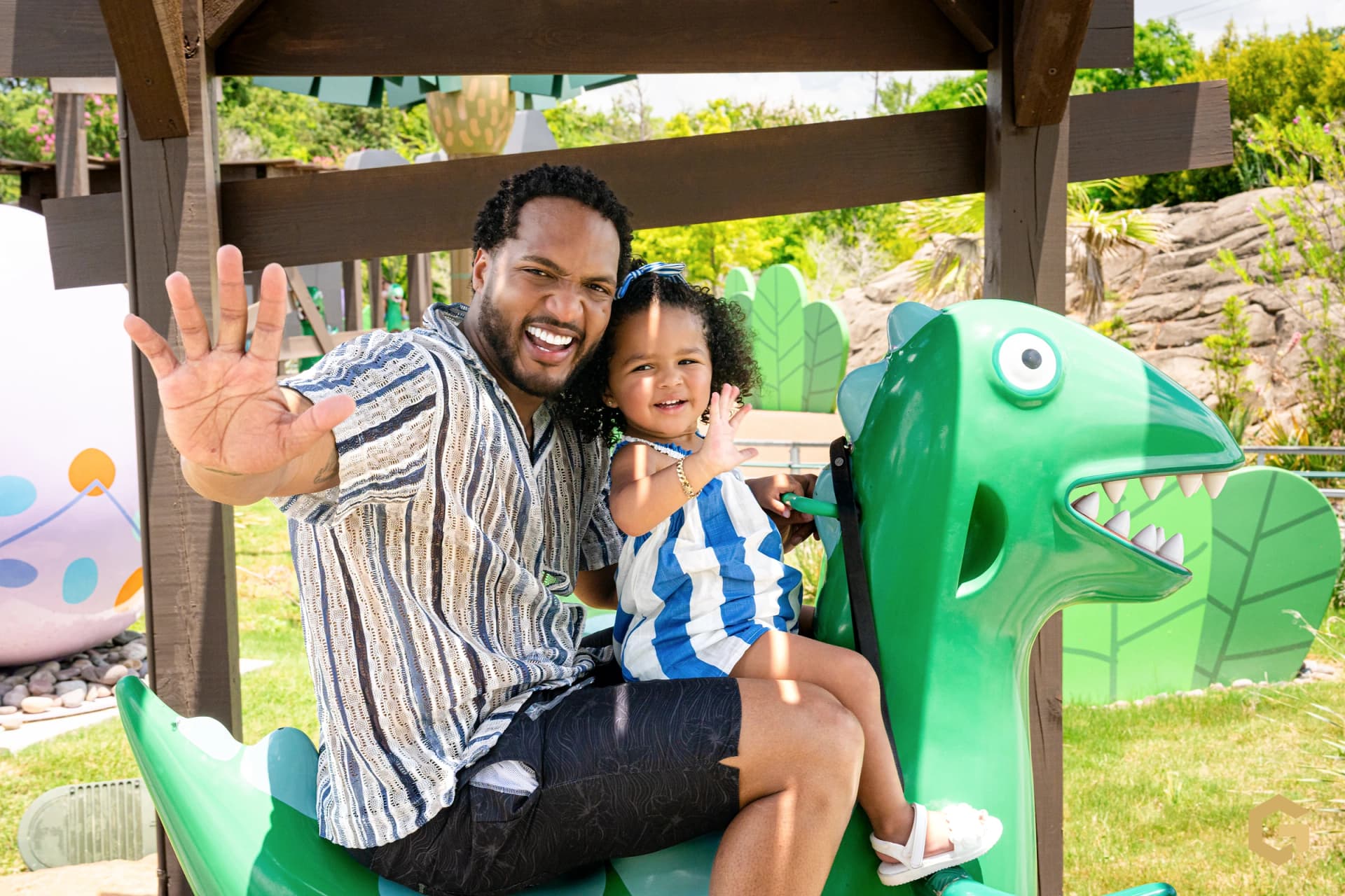 Edgardo and his daughter waving from the green dinosaur ride