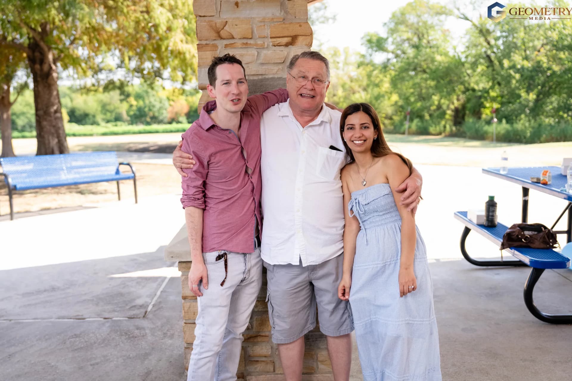 The couple embrace a family member beneath the pavilion