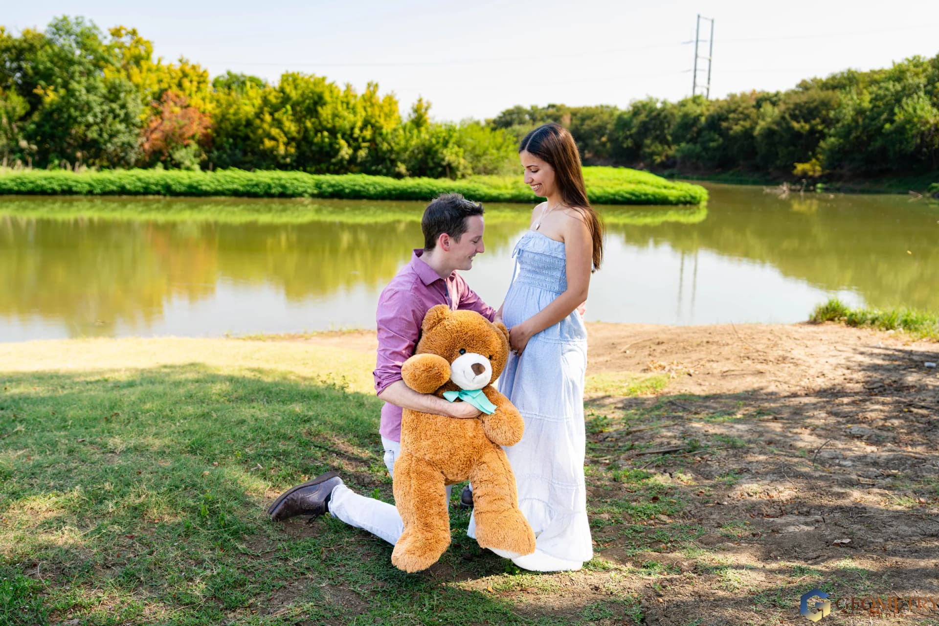 The couple share a quiet maternity moment beside the lake with a teddy bear