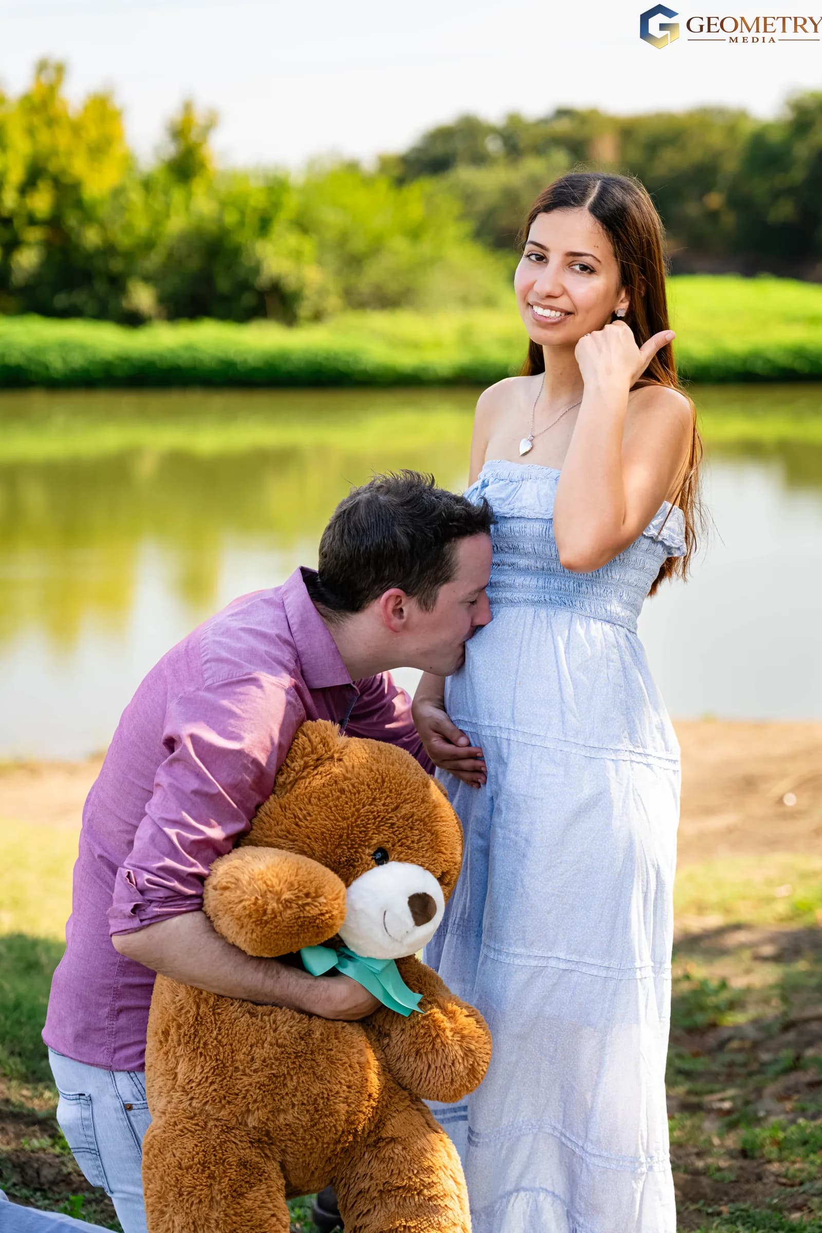 Father kisses the baby bump during a lakeside maternity portrait