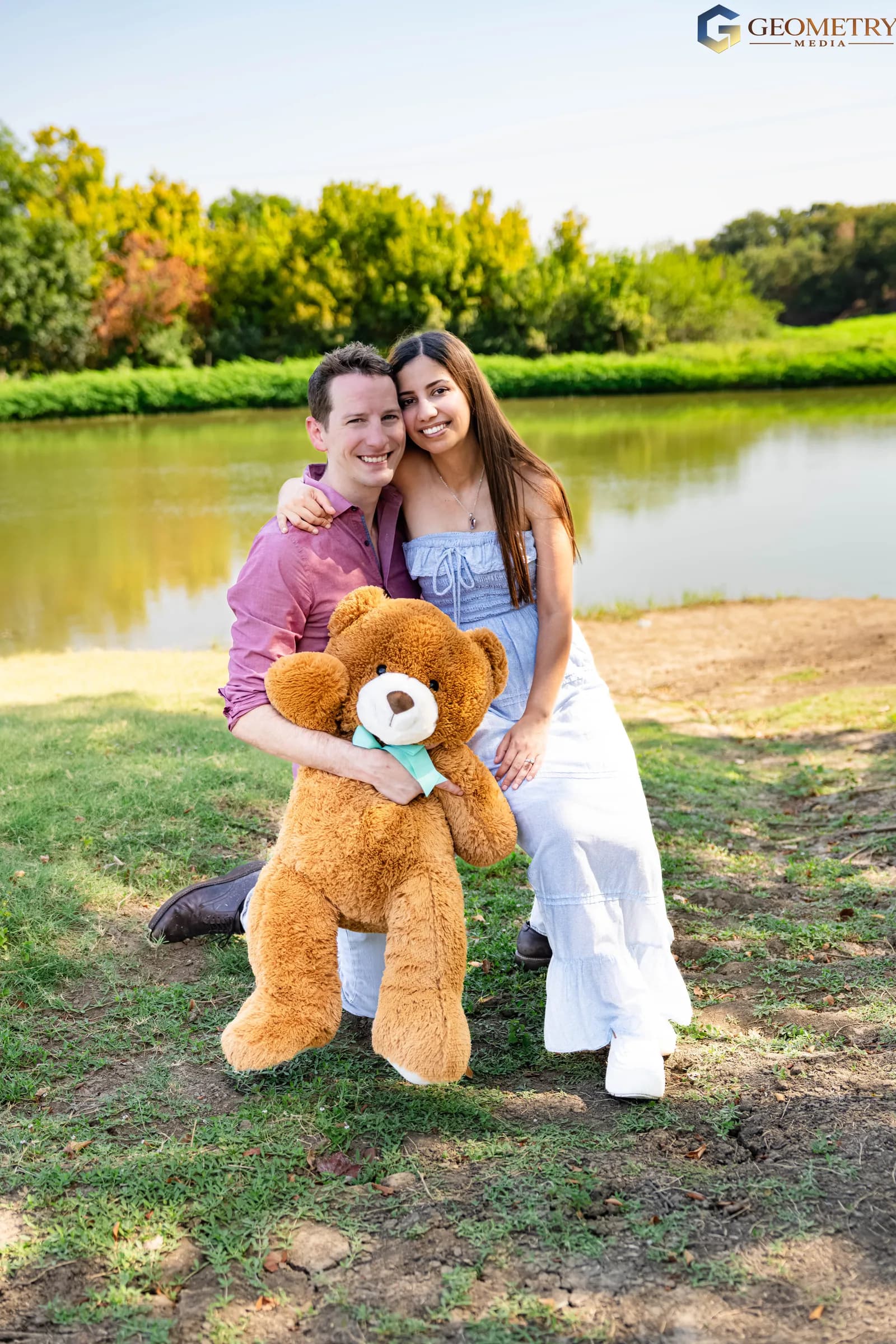The couple smile together holding a teddy bear after the reveal
