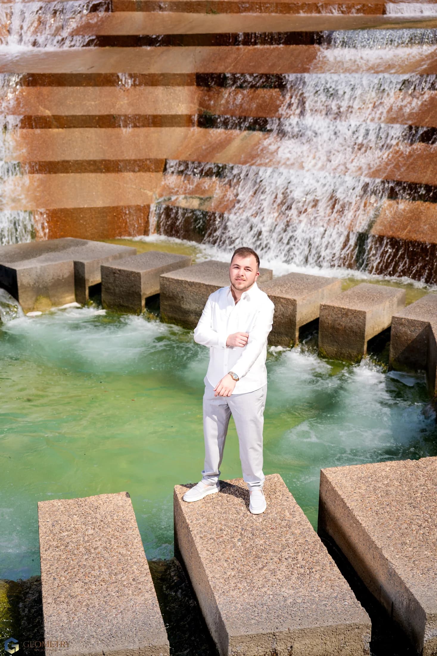Full-length groom portrait beside the fountain
