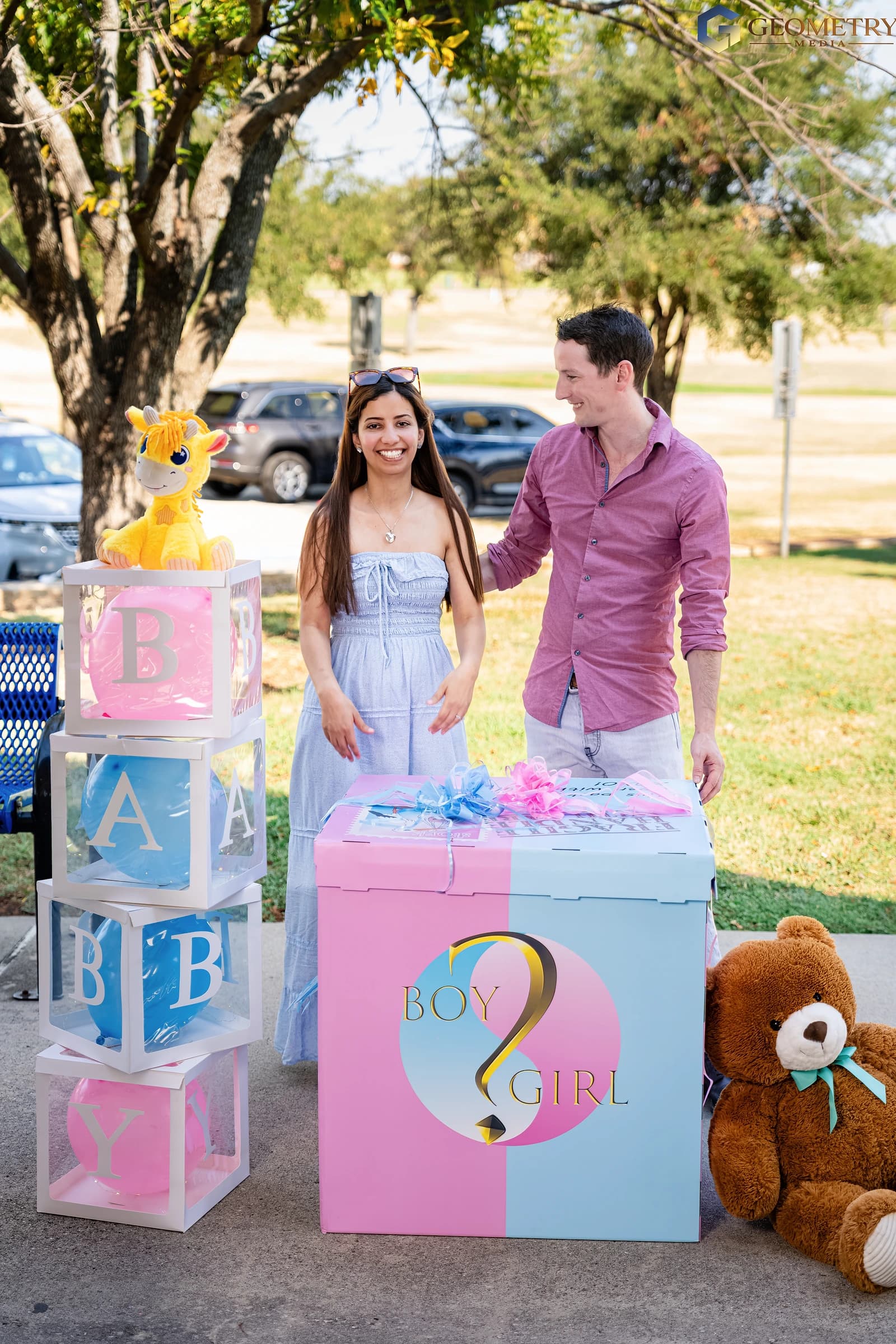 Couple smiling beside the pink-and-blue reveal box at Israa’s gender reveal party